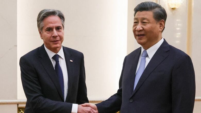 Two men in navy suits shake hands while posing for a photo.