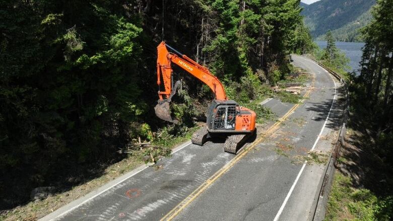 An orange machine clears debris from a highway along a lake.