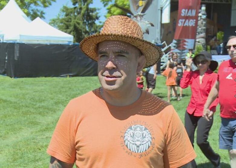 Indigenous man in an orange Every Child Matters shirt and straw hat. 