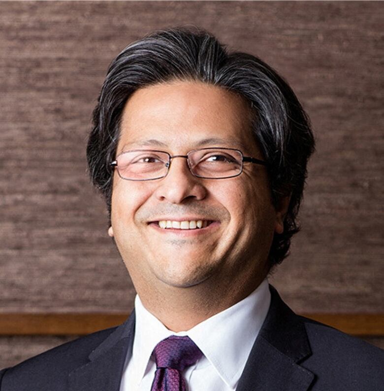 A man with black hair smiling at the camera. He's wearing a suit.