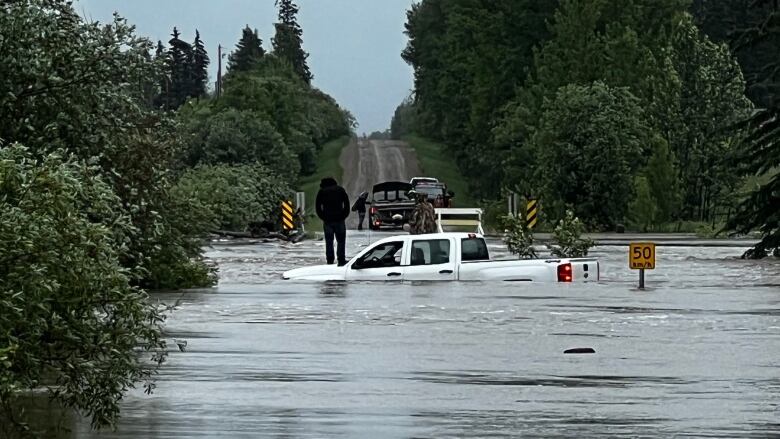 A person stands on top of a white truck surrounded by floodwaters