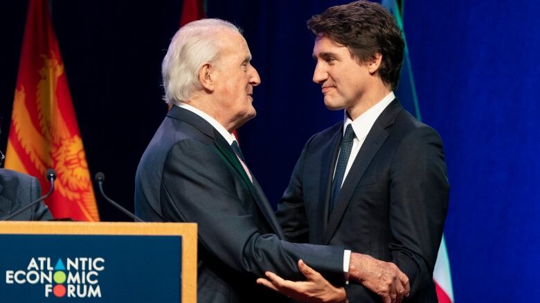 Prime Minister Justin Trudeau and former prime minister Brian Mulroney embrace on stage at an event in Antigonish, N.S.