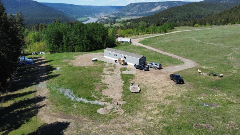 An aerial photo shows a property, mostly green grass field with a small mobile home in the centre and a few vehicles scattered. 