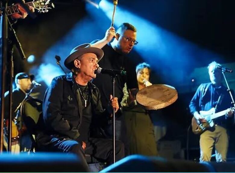 A group of men sing and bang on drums.