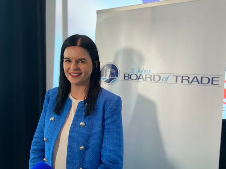 A person with long dark hair in a blue suit stands in front of a St. John's Board of Trade sign.