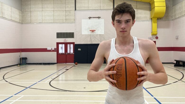 Tyson Christensen who plays for team Manitoba's U19 Basketball Team stands on court gripping a basketball between two hands.