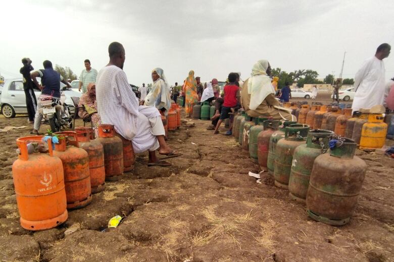 Lines of orange, green and yellow propane tanks are shown in a field, with people milling about.