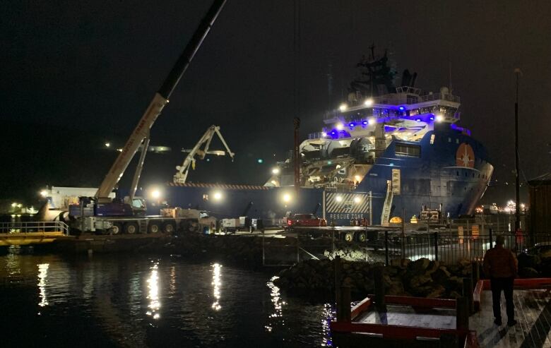 Cranes loading crates onto a large blue ship.