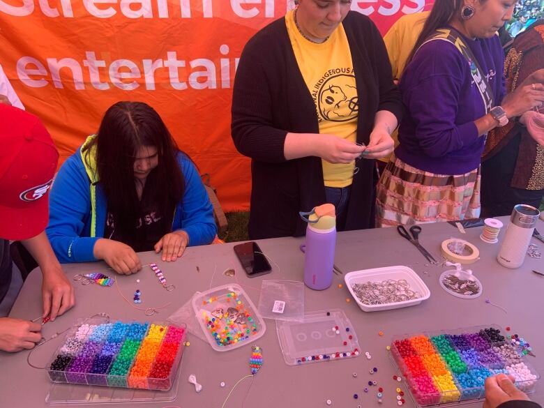 A person in a blue sweater works with beads at a table with colourful beading supplies on it.