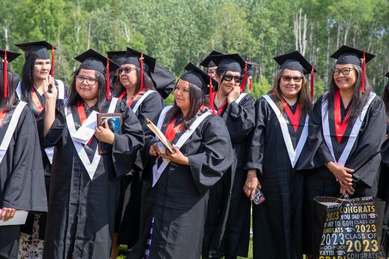 Women in graduation gowns stand outside.