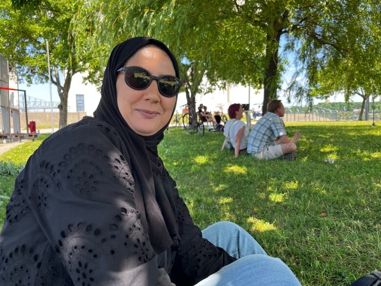 A woman wearing sunglasses and a black headscarf smiles at the camera.