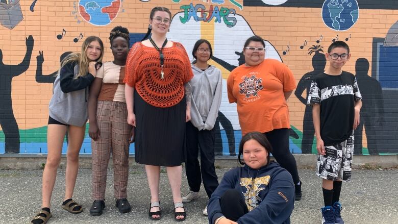 A teacher and a group of pre-teens pose in front of a mural.