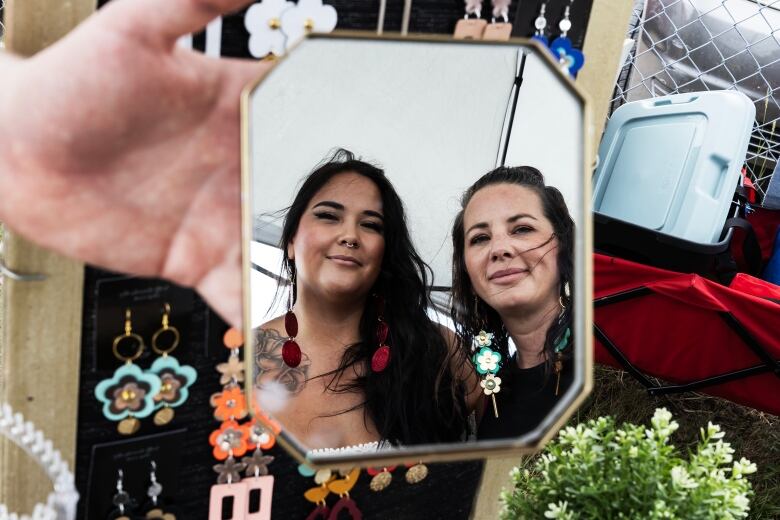 Two women are pictured in the reflection of a handheld mirror.