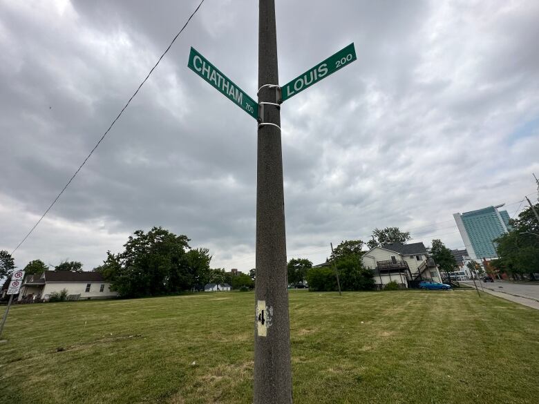 Street signs are shown in front of a plot of green land.