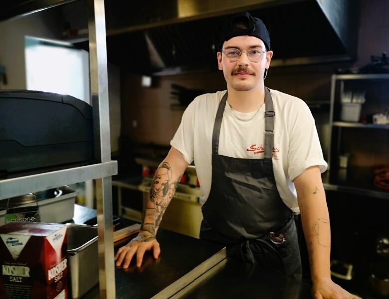 Zac Berry stands in the kitchen wearing a black apron over a white t-shirt