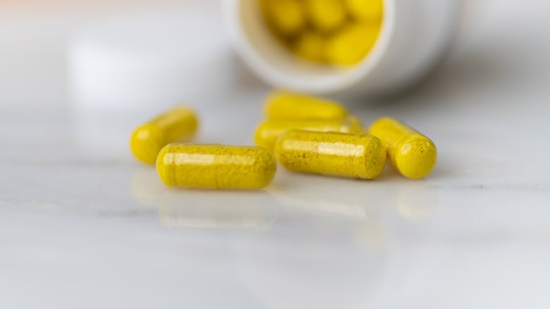 Yellow capsules of a supplement called berberine w/ bottle in the background.