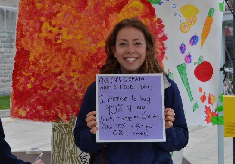 A woman smiles at a camera while holding up a sign that says 