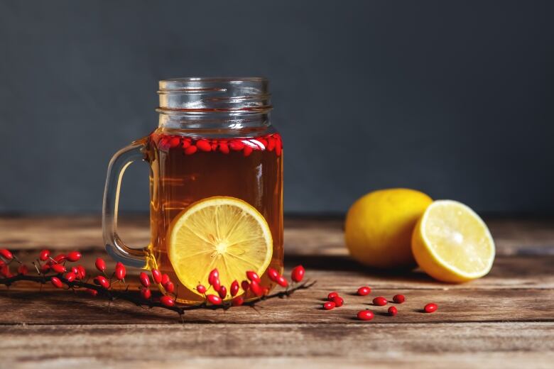 A clear mug of barberry tea with sliced lemon and berry branches sitting on a table.