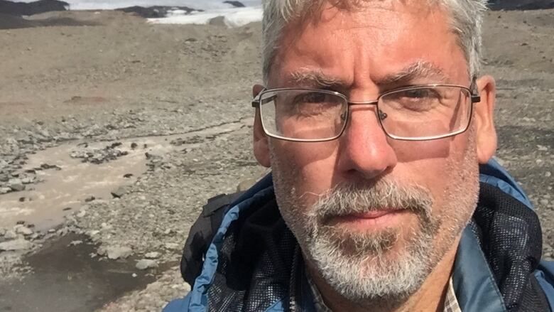 A bearded man poses for a selfie in a barren landscape.