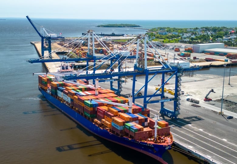 Two massive cranes begin unloading crates off of a large ship. 