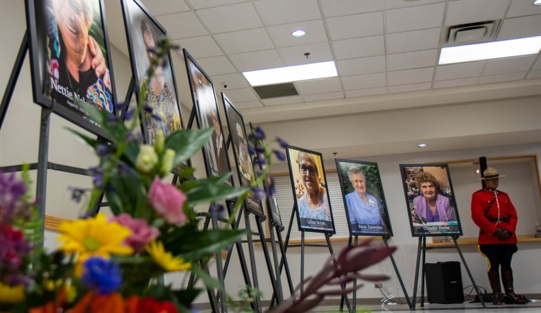 A row of photos of people, flanked on one side by flowers and on the other side by a uniformed RCMP officer.