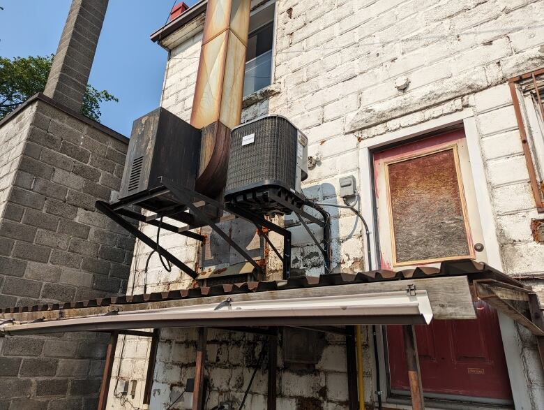 An air conditioner attached to the back of a white brick building.