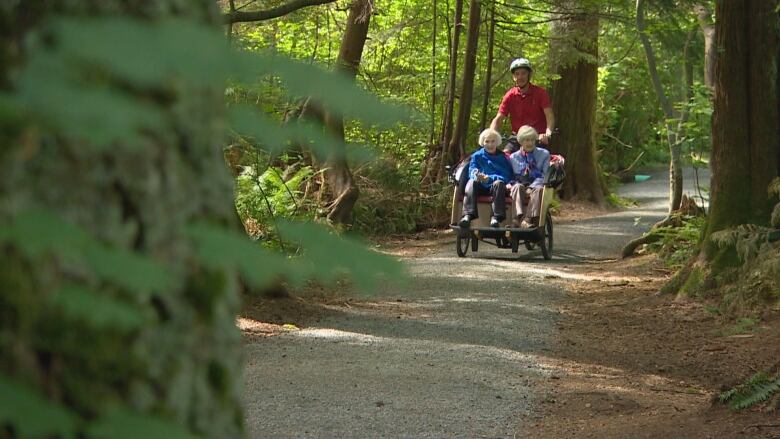   A man pedals a three-wheeled bicycle with two senior women in the passenger chariot