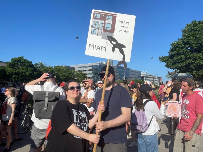 Eli San and her partner holding a protest sign showing an orca eating a condo