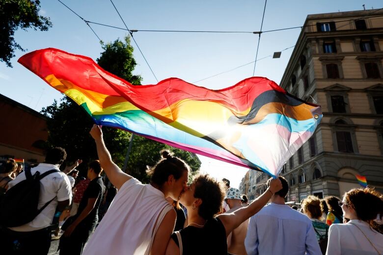 Two men kissing while holding a flag at a Pride parade in Rome.