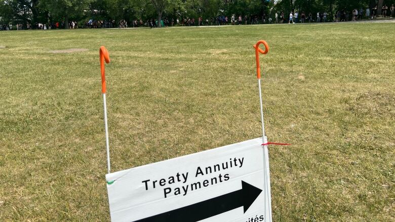 A long lineup of people is pictured in the distance. Nearby, a sign that says 'Treaty Annuity Payments' with an arrow is shown.