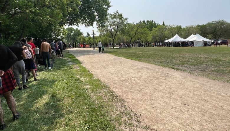 A long lineup of people is shown leading up to a white tent in the distance.