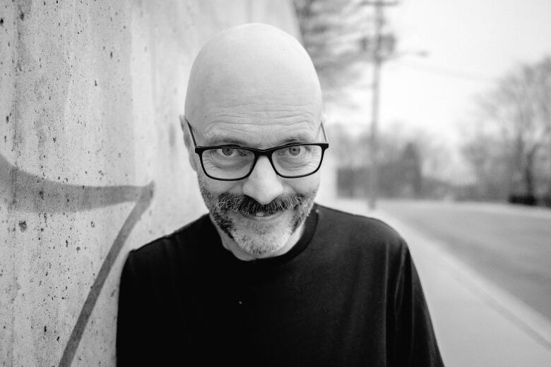 A man wearing a black sweater leaning against a concrete wall. 