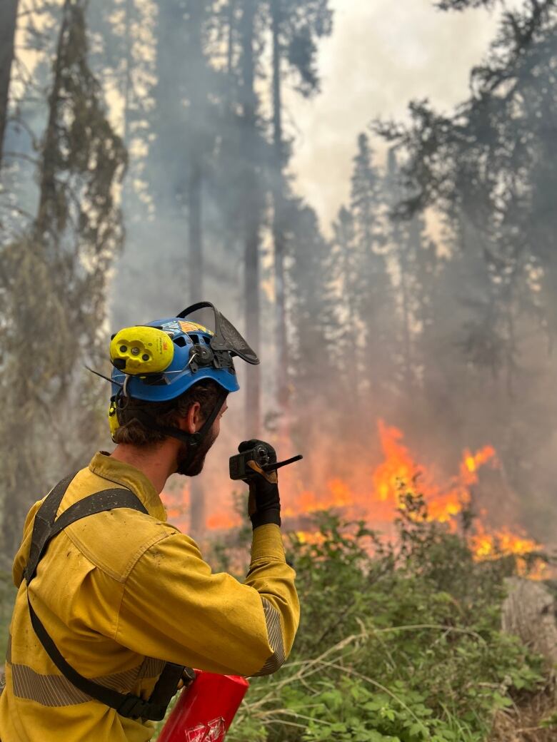 Man speaking into walkie talkie, trees, flames. 