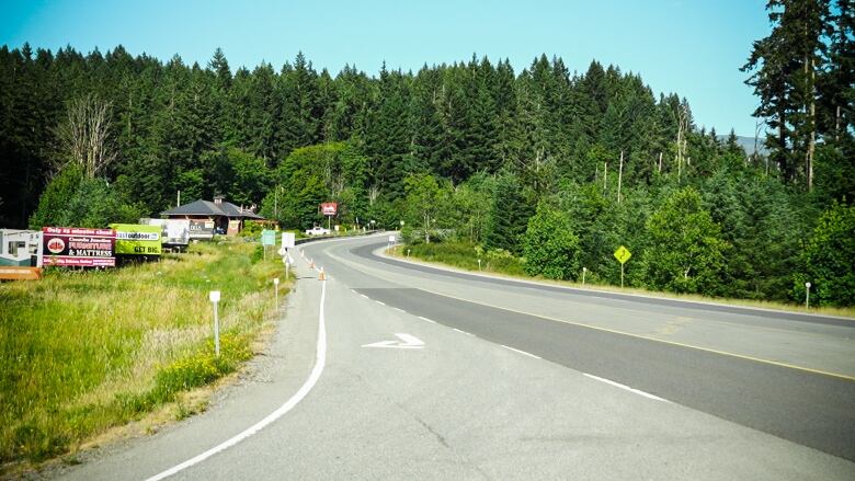 An empty highway stretches into the forest in the distance, with a few houses.