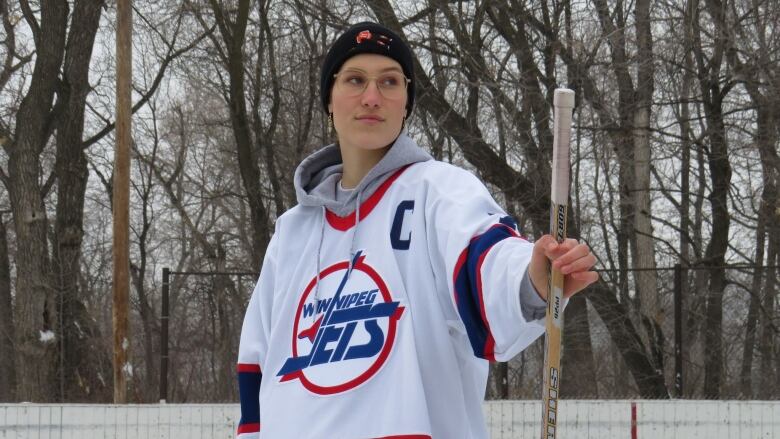 A person in a hockey jersey stands on a rink holding a hockey stick.