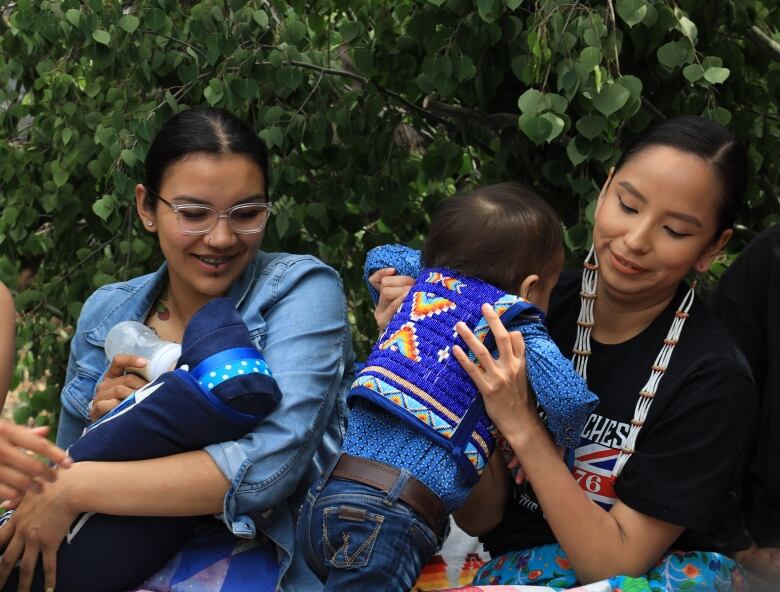 Mothers Martina Desjarlais (left) and Maelan Tsatoke (right) hold their children during their placenta ceremony. 