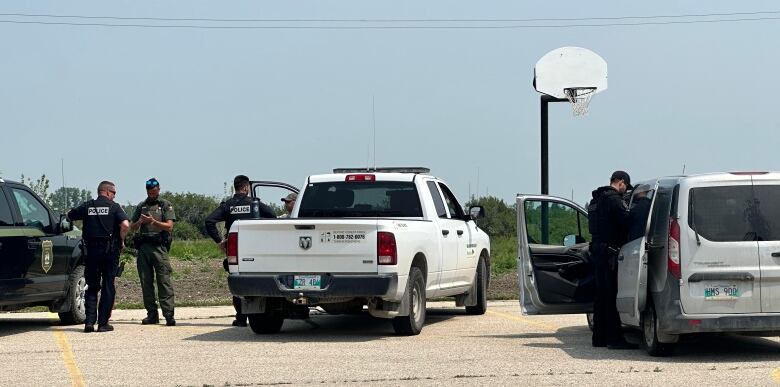 Uniformed men gather around a number of trucks in a parking lot on a sunny day. 