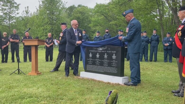 Two men lift a curtain off the memorial. 