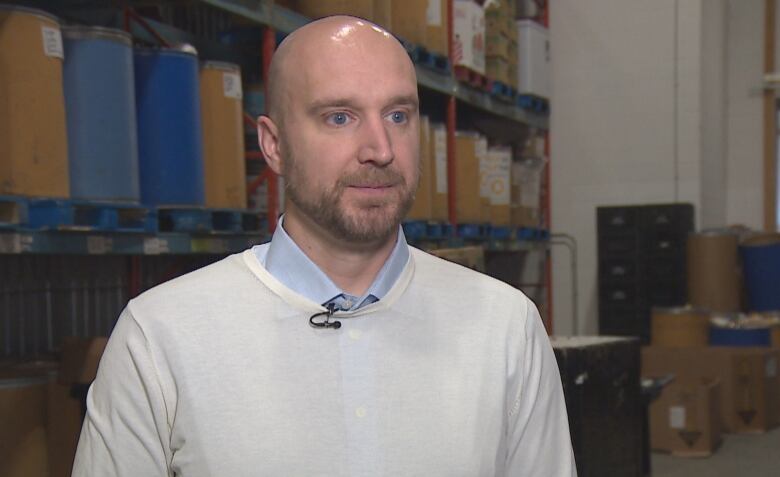 A bald man in a white sweater is standing in a warehouse. 