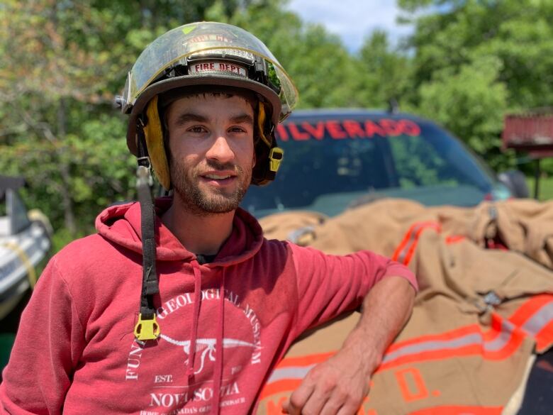 Eric Jeffery is a fisherman and volunteer with the Gunning Cove fire department. He stands beside his black truck, wearing a firefighter helmet. 