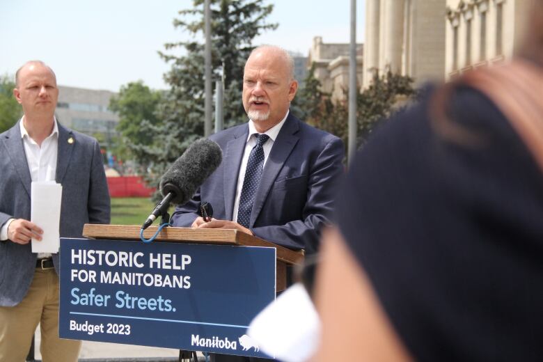 A politician speaks into a microphone at a podium outside at a government news conference.