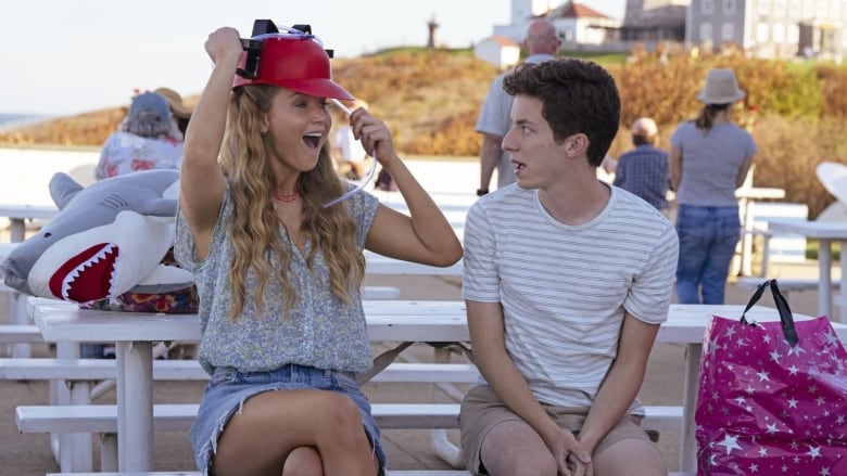 A woman wears a helmet-like hat with a straw attached as the young man next to her looks on in surprise.