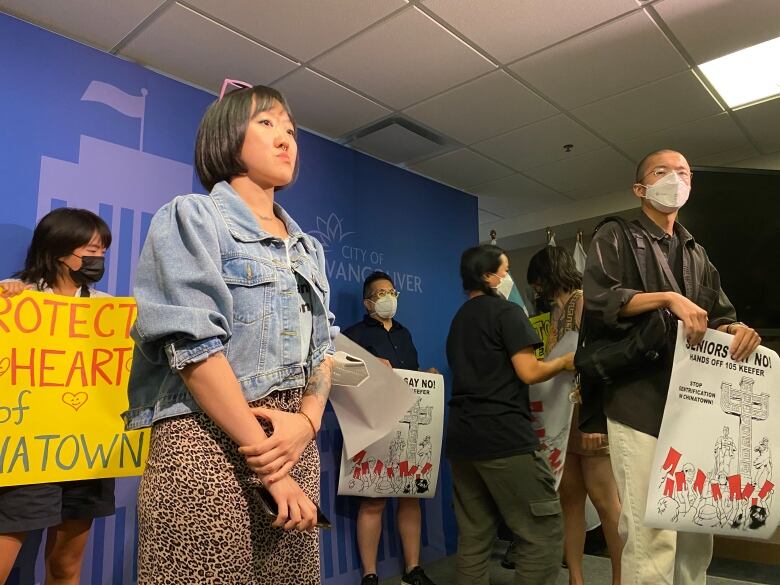 Protesters at Vancouver city hall hold up placards in an indoor environment.