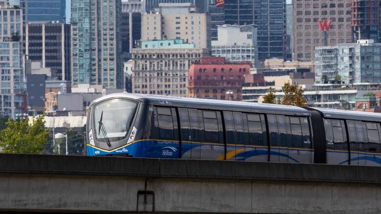 A light rail train passing in front of a downtown skyline.