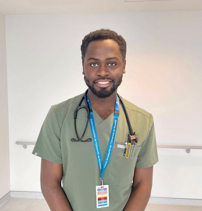 A young Black man wearing green scrubs, a lanyard and a stethoscope around his neck.