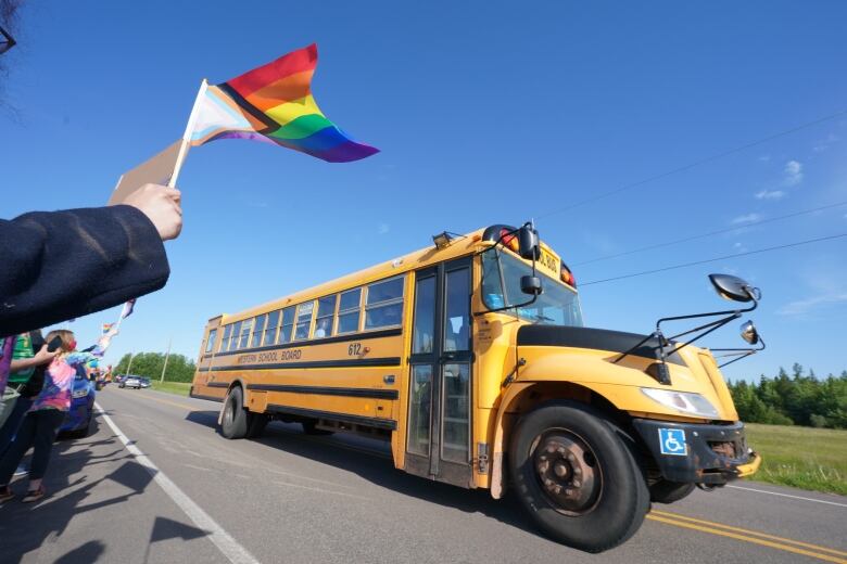 People wave LGBTQ Pride flags as a school bus drives by