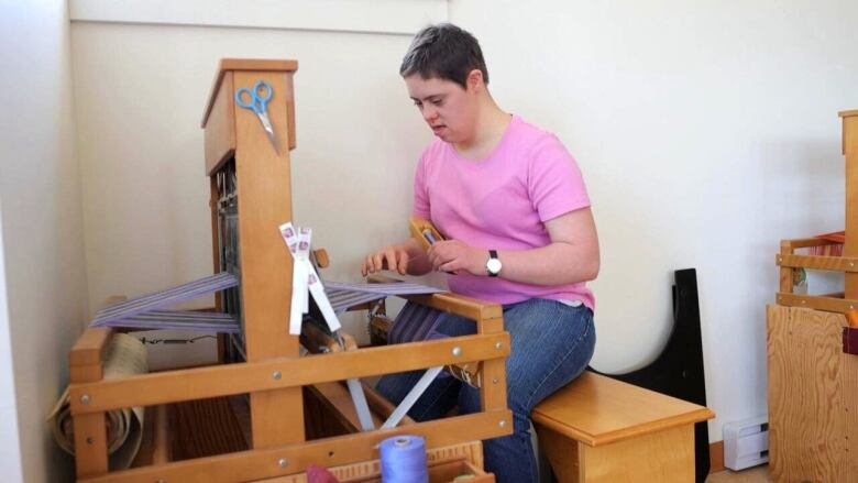 A person in a pink shirt works on a weaving loom.