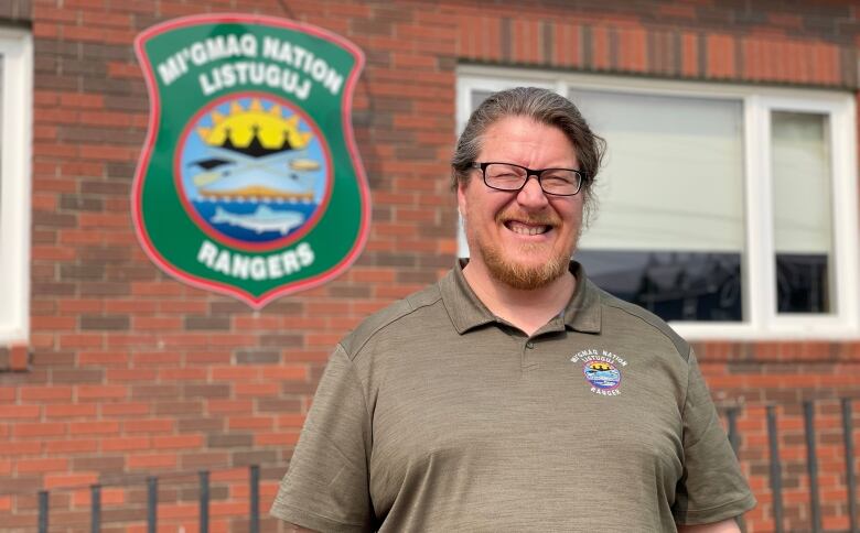 A man smiling outside a brick building with a green crest on it that says 