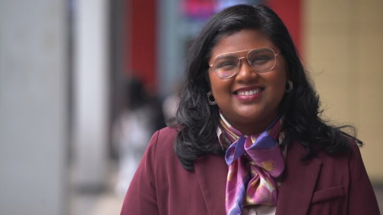 A woman with glasses smiles with a blurred background.