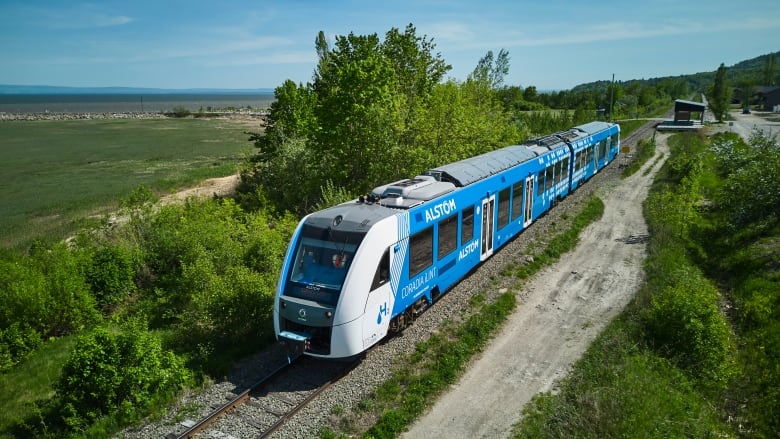 A blue and white train travels across the countryside, as viewed from the air